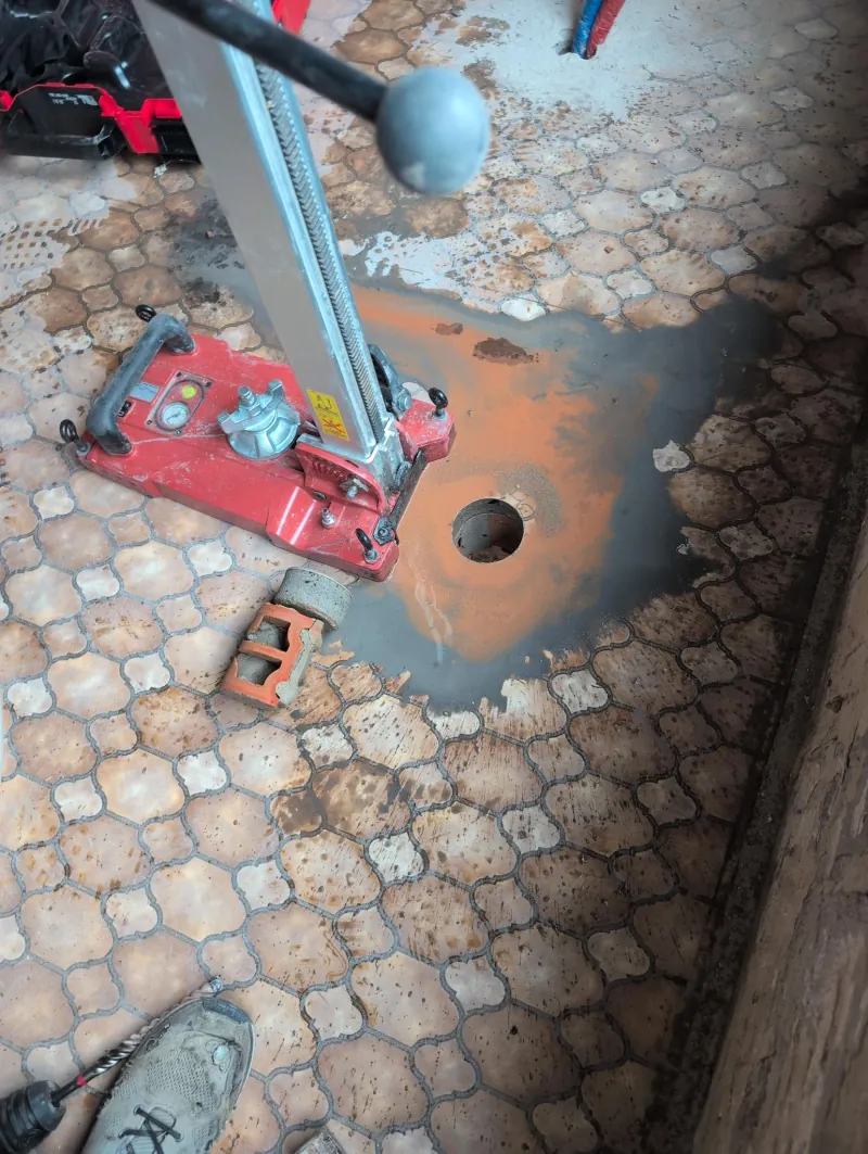 Kernboring door de vloer voor de afvoer van de douche, met de boorkern naast het statief