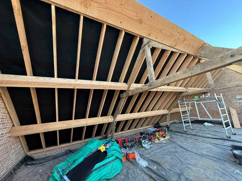 Nieuwe dakconstructie van binnenuit, met houten kepers en gordingen tegen het zwarte onderdak