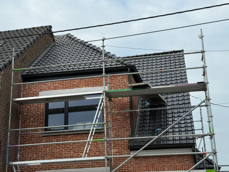 Hellend dak met nieuwe dakpannen en zwarte dakranden, gezien vanaf de stelling