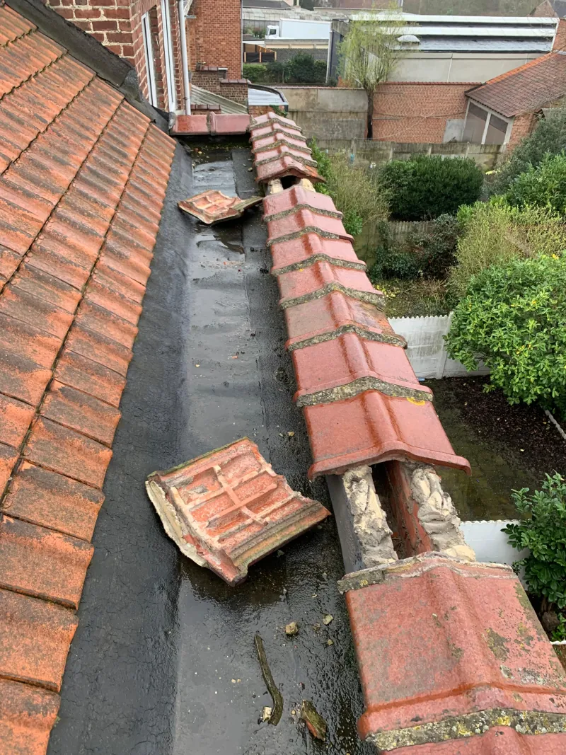 Losgekomen muurkappen op een plat dak naast een pannendak, na stormschade