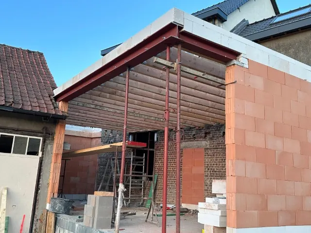Aanbouw in ruwbouw met rode stalen liggers op stempels en nieuw metselwerk in snelbouwsteen
