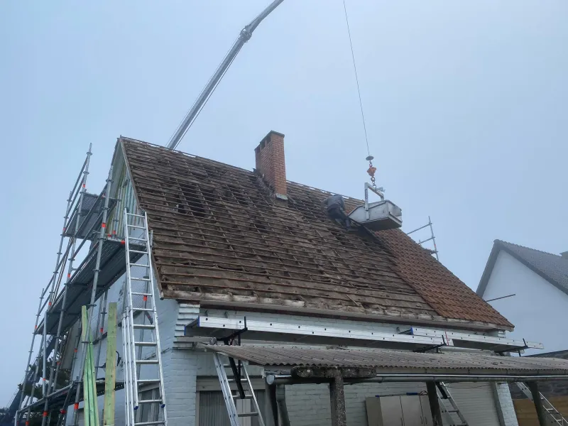 Oude rode pannen worden van het dak gehaald, met een kraanbak naast de nok